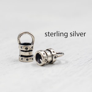 May include: Two sterling silver barrel-shaped beads with a loop at the top. Each bead has three sections with decorative markings. The text "sterling silver" is visible in the image.