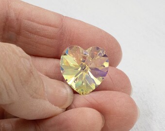 May include: A heart-shaped crystal pendant with a yellow and iridescent finish. The pendant is held in a hand, showcasing its faceted design and light refraction. The crystal reflects a spectrum of colors.
