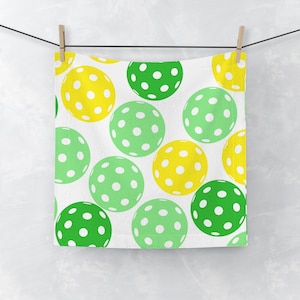 May include: A white kitchen towel with a repeating pattern of green and yellow pickleball balls. The balls have white dots.