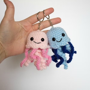 May include: Two crocheted jellyfish keychains, one pink and one blue, with smiling faces and dangling tentacles.