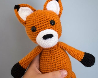 May include: A crocheted orange fox plush toy with black eyes, a white nose, and black tipped ears and paws.