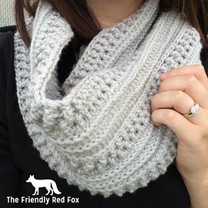 May include: A gray crocheted infinity scarf with a textured pattern. The scarf is worn by a person and the image includes the text "The Friendly Red Fox".