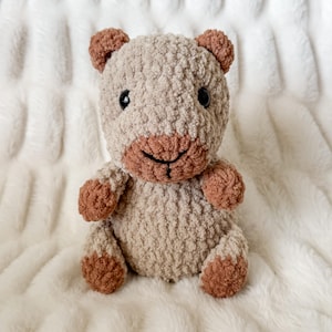 Puede incluir: Un oso de peluche hecho a mano, en tonos beige y marrón. El oso tiene un aspecto texturizado y difuso con acentos marrones en las orejas, el hocico y las patas. Presenta ojos de seguridad negros y una sonrisa cosida. El oso está sentado erguido.