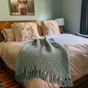 Chunky crochet blanket in soft, thick yarn showcasing cozy, textured stitches perfect for beginners. Draped gently over a sofa, ideal size for home decor accents. PDF crochet pattern with video tips included for easy crafting