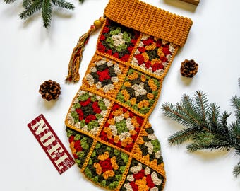 May include: A handmade Christmas stocking with a granny square design in shades of red, green, yellow, and cream. The stocking has a mustard yellow cuff and loop, with a tassel. The word "believe" is on a small wooden sign.