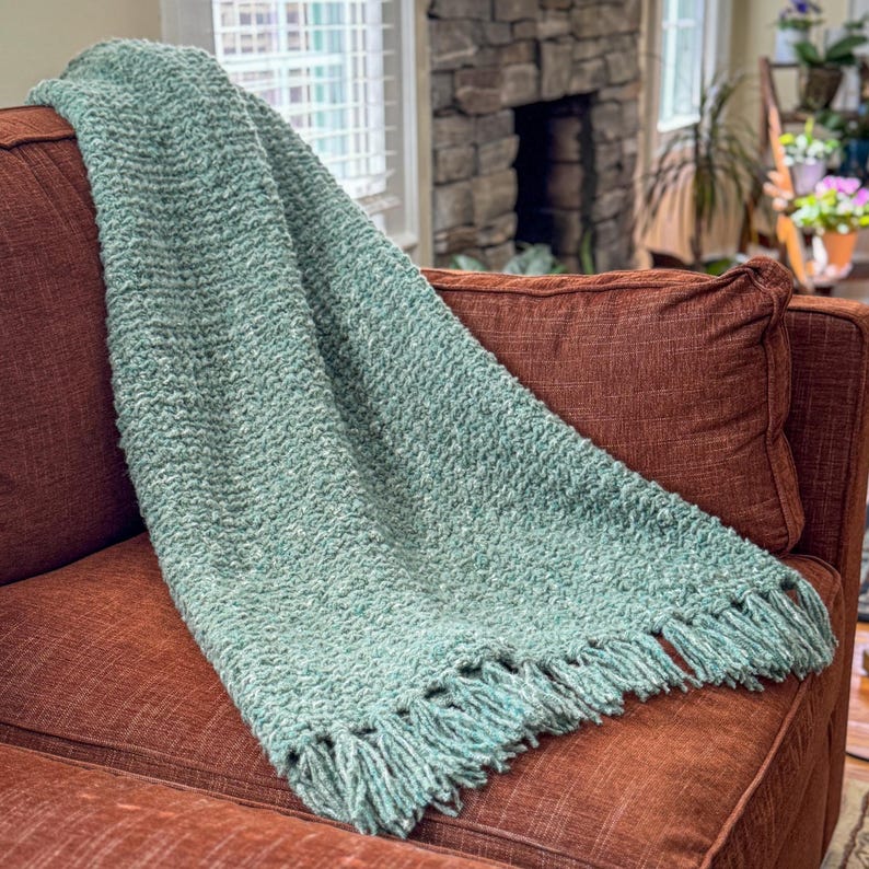 Chunky crochet blanket in soft, thick yarn showcasing cozy, textured stitches perfect for beginners. Draped gently over a sofa, ideal size for home decor accents. PDF crochet pattern with video tips included for easy crafting