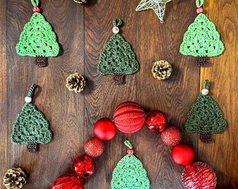 May include: A festive arrangement featuring crocheted Christmas tree ornaments in shades of green, accented with red and white beads. Red and glittery ornaments and pinecones are arranged on a wooden surface, with a wire star.