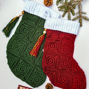 Könnte beinhalten: Zwei handgefertigte Weihnachtsstrümpfe, einer grün und einer rot, mit weißen Bündchen. Die Strümpfe sind mit einem quadratischen Muster gehäkelt. Jeder Strumpf hat eine Quaste und eine Schlaufe zum Aufhängen. Das Wort "NOEL" ist sichtbar.