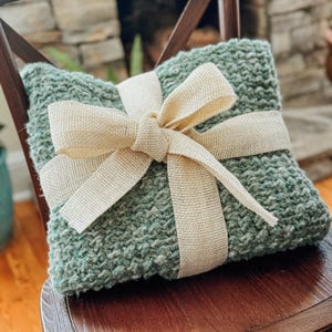 Chunky crochet blanket in soft, thick yarn showcasing cozy, textured stitches perfect for beginners. Draped gently over a sofa, ideal size for home decor accents. PDF crochet pattern with video tips included for easy crafting