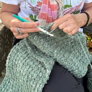 Chunky crochet blanket in soft, thick yarn showcasing cozy, textured stitches perfect for beginners. Draped gently over a lap, ideal size for home decor accents. PDF crochet pattern with video tips included for easy crafting