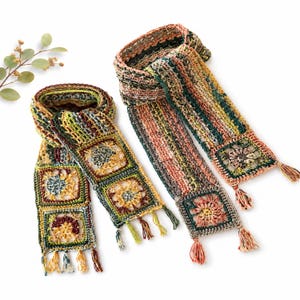 May include: Two handmade crochet scarves featuring a mix of earthy tones including green, yellow, rust, and brown. Each scarf is constructed with a series of square floral motifs and textured striped sections, finished with small decorative tassels.