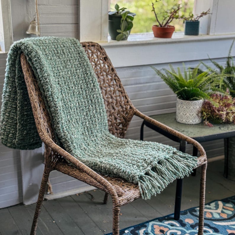 Chunky crochet blanket in soft, thick yarn showcasing cozy, textured stitches perfect for beginners. Draped gently over a sofa, ideal size for home decor accents. PDF crochet pattern with video tips included for easy crafting