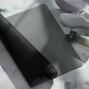 Puede incluir: Una esterilla de yoga negra enrollada sobre una superficie gris con una botella de agua blanca y zapatillas blancas.