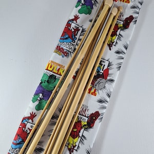 May include: A set of six wooden knitting needles in a fabric bag with a comic book print featuring characters like Hulk, Spiderman, and Iron Man. The bag has a black drawstring.