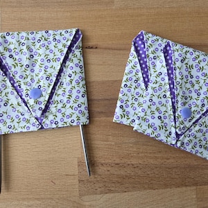 May include: Two needle cases with a floral pattern in white, purple, and green. The cases are folded and secured with a purple button. The interior lining is purple with white polka dots. The needles are silver.
