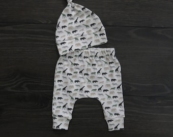 May include: A white baby hat and pants set with a print of various safari animals, including giraffes, zebras, and rhinoceroses.