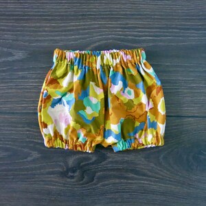 May include: A pair of colorful baby bloomers with a floral print in shades of brown, green, blue, pink, and white.