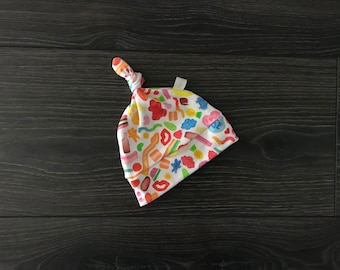 May include: A white baby hat with a knot on top. The hat is covered in a colorful pattern of candy and sweets. The text "I love you" is printed on the hat.