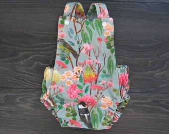May include: A baby romper with a floral print featuring birds and flowers. The romper is made of a soft, lightweight fabric and has a ruffled hem.