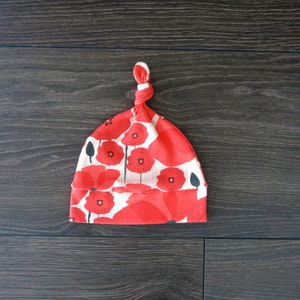 May include: Red and white baby hat with a poppy flower pattern. The hat is tied at the top with a knot.