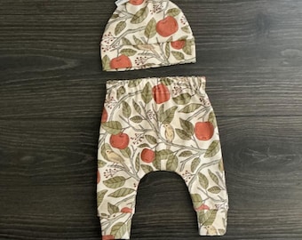 Conjunto orgánico para bebé: pantalones bombachos con estampado de manzanas y gorro con nudo.