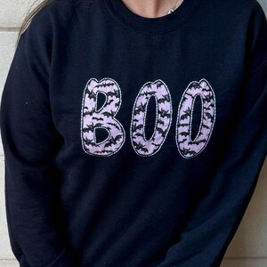 May include: Black sweatshirt with a pink "BOO" graphic made of bats.