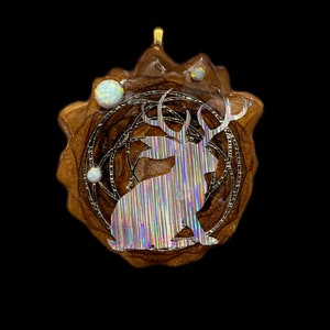 May include: A wooden pendant with a silver iridescent deer silhouette inside a circular design. The pendant has a gold bail and is surrounded by small white opals.