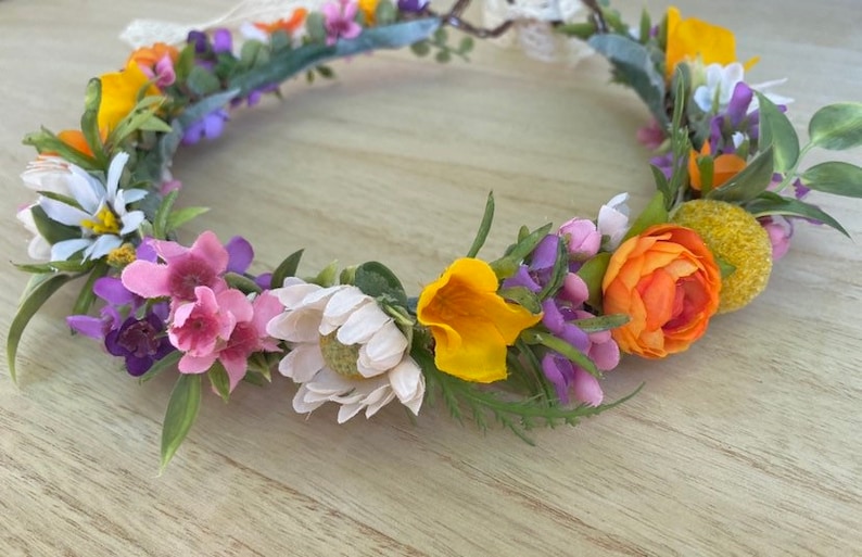 May include: A floral crown with a variety of flowers, including white, pink, purple, yellow, and orange. The crown is made of artificial flowers and greenery.