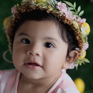 May include: A young child wearing a flower crown with pink and yellow flowers. The crown is made of natural materials and has a rustic look.
