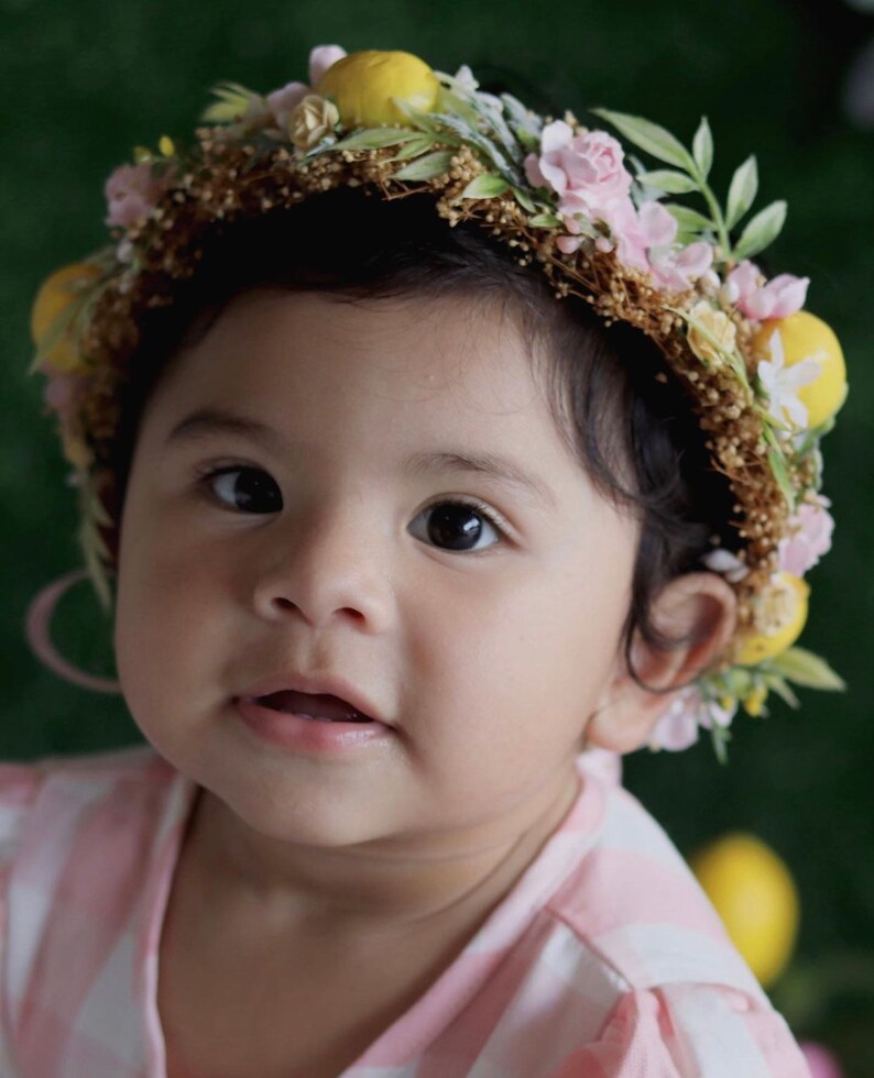 May include: A young child wearing a flower crown with pink and yellow flowers. The crown is made of natural materials and has a rustic look.