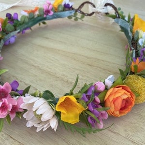May include: A floral crown with white, pink, purple, orange, and yellow flowers. The crown is made of artificial flowers and greenery.