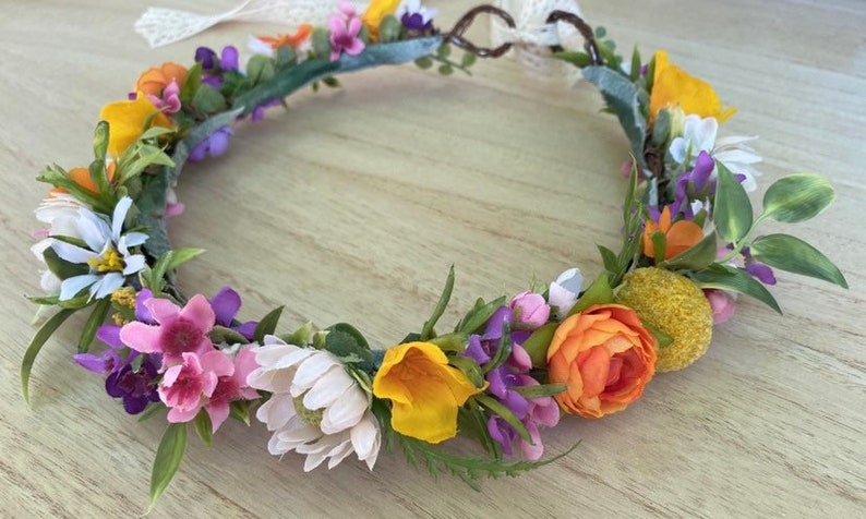 May include: A floral crown with white, pink, purple, orange, and yellow flowers. The crown is made of artificial flowers and greenery.