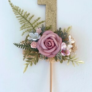 K&ouml;nnte beinhalten: Goldener Glitzer-Nummer-Eins-Kuchentopper mit rosa und wei&szlig;en Blumen und Gr&uuml;n.