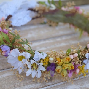 May include: A floral crown made of white, yellow, purple, and pink flowers. The crown is made of dried flowers and greenery.