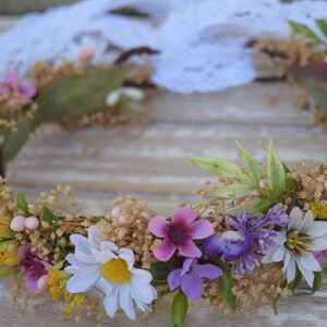 May include: A floral crown made of white, yellow, pink, and purple flowers. The crown is made of dried flowers and greenery and is perfect for a wedding or other special occasion.