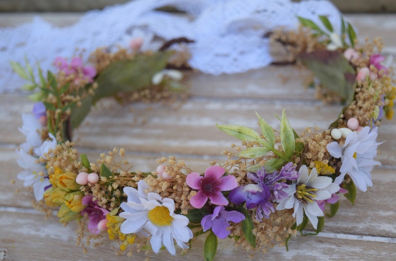 May include: A floral crown made of white, yellow, pink, and purple flowers. The crown is made of dried flowers and greenery and is perfect for a wedding or other special occasion.