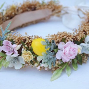 May include: A floral crown with pink and white flowers, green leaves, and yellow lemons. The crown is made of dried flowers and is perfect for a summer wedding or festival.