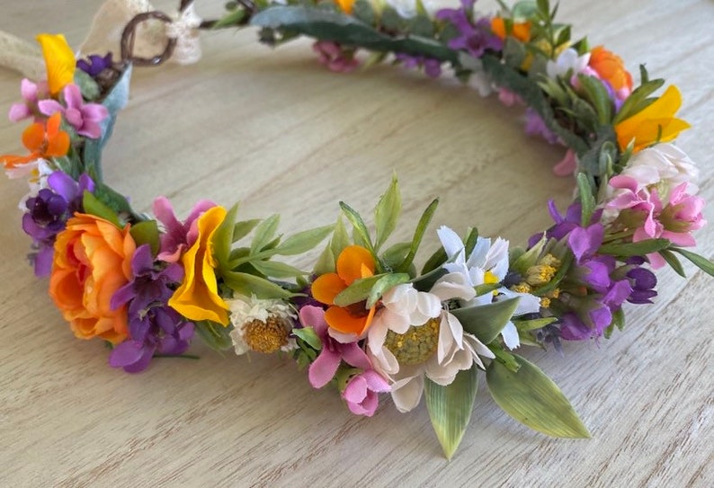 May include: A floral crown with orange, yellow, white, pink, and purple flowers. The crown is made of artificial flowers and greenery.