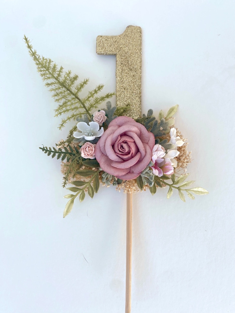 K&ouml;nnte beinhalten: Goldener Glitzer-Nummer-Eins-Kuchentopper mit einer rosa Rose und Gr&uuml;n.