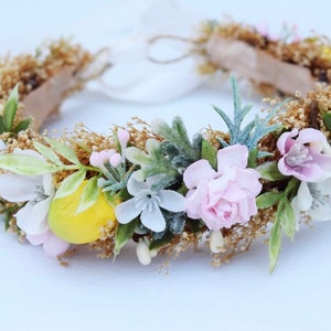 May include: A floral crown with pink, white, and yellow flowers, green leaves, and a brown base.