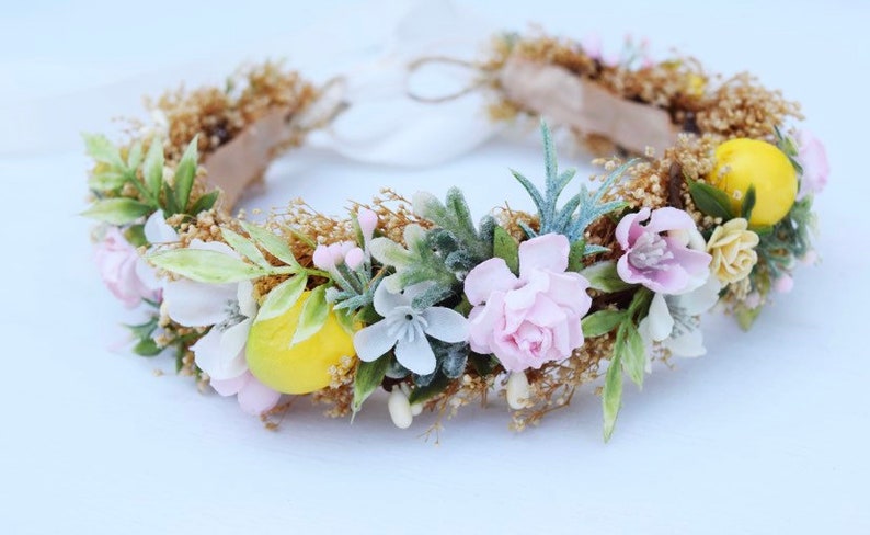 May include: A floral crown with pink, white, and yellow flowers, green leaves, and a brown base.