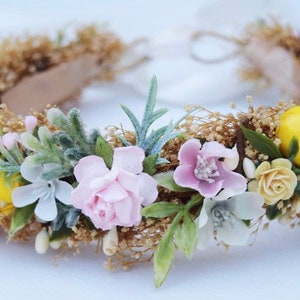 May include: A delicate floral crown with pink and white flowers, green leaves, and yellow lemons. The crown is made with a brown base and is perfect for a special occasion.