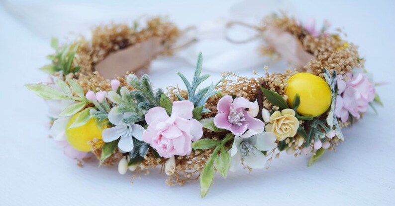 May include: A delicate floral crown with pink and white flowers, green leaves, and yellow lemons. The crown is made with a brown base and is perfect for a special occasion.