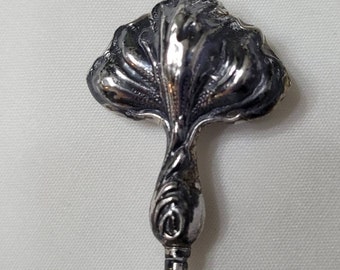May include: A silver-toned floral design hat pin with a long, thin pin. The pin is made of metal and has a detailed floral design.