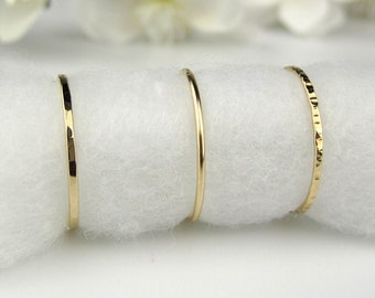 May include: Three gold stacking rings on a white background. The rings are different widths and textures. The ring on the left is smooth, the middle ring is smooth, and the ring on the right has a textured surface.