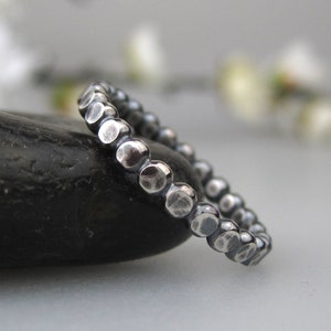 May include: A silver ring with a hammered texture, featuring a series of small, round beads.
