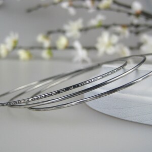 May include: Three silver bangle bracelets with a hammered texture. The bracelets are stacked on top of each other.
