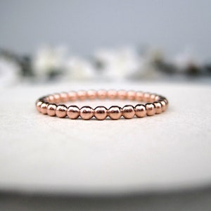 May include: A rose gold beaded ring. The ring is made of small, round beads that are evenly spaced.