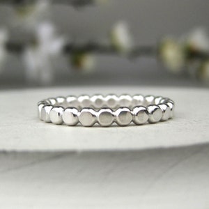 May include: A silver ring with a beaded design. The ring is made of small, round beads that are evenly spaced around the band.