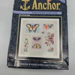 May include: An Anchor Hardanger Made Easy 28111 Butterfly Collage embroidery kit package. The dark blue box features a cross-stitch pattern of various butterflies and flowers. It measures approximately 7 inches by 7 inches as stated on the box.